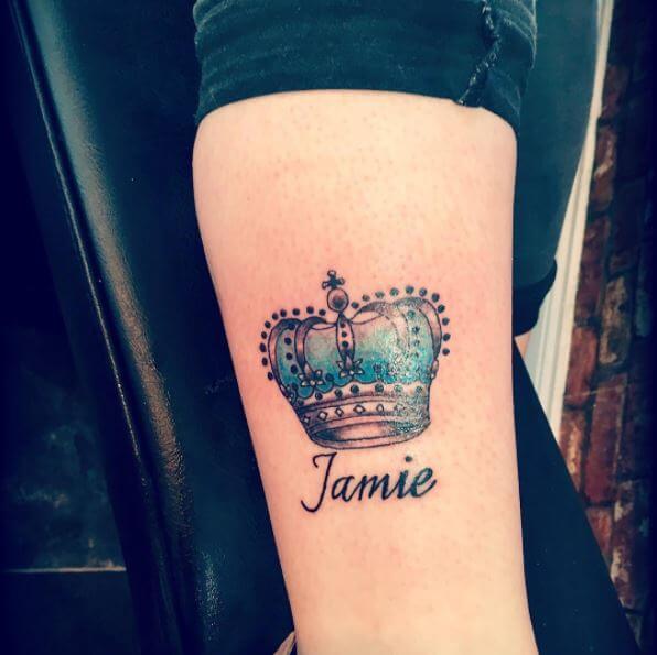 Tatuaje en el antebrazo, nombre de Jamie Queen y corona