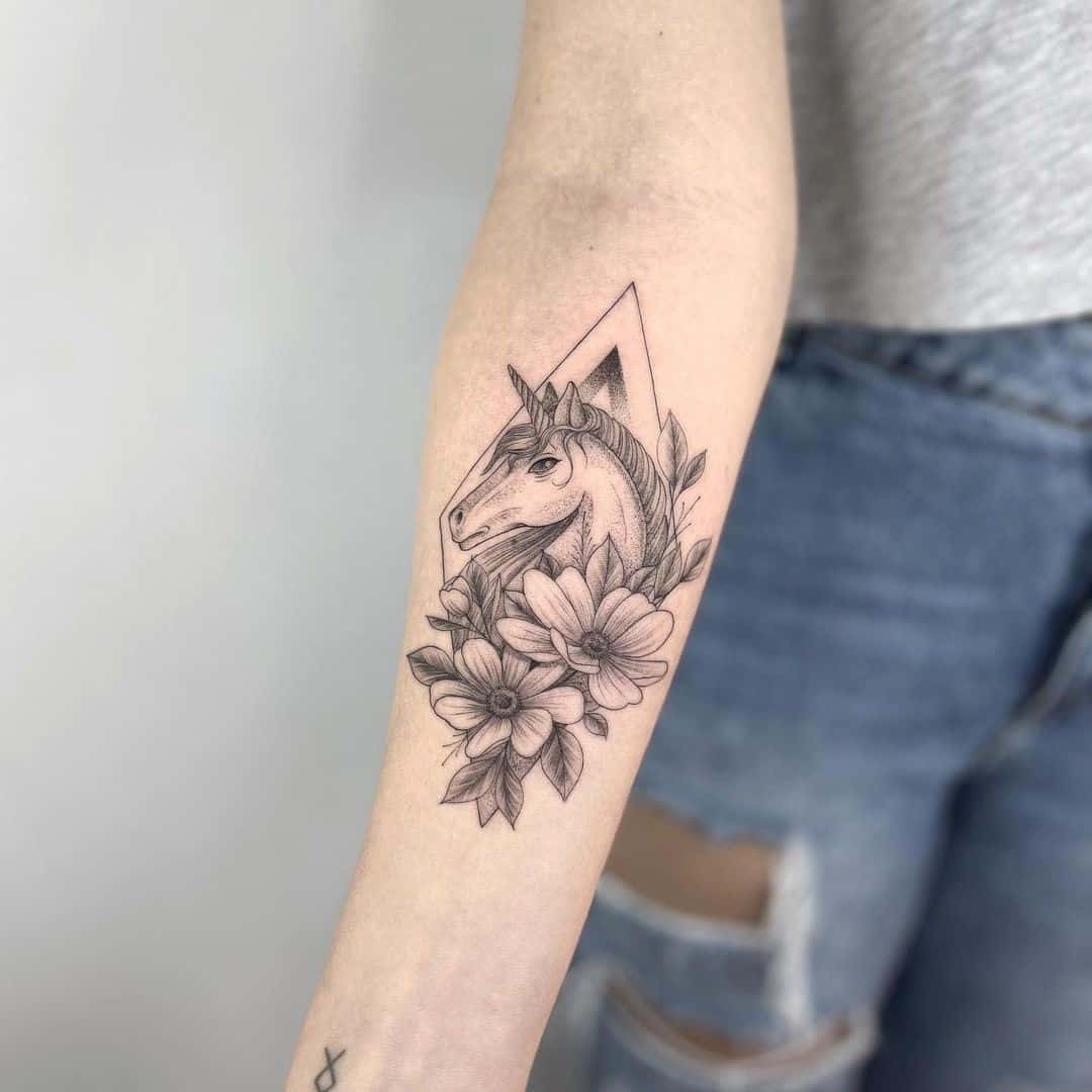 Tatuaje de unicornio negro con flores.