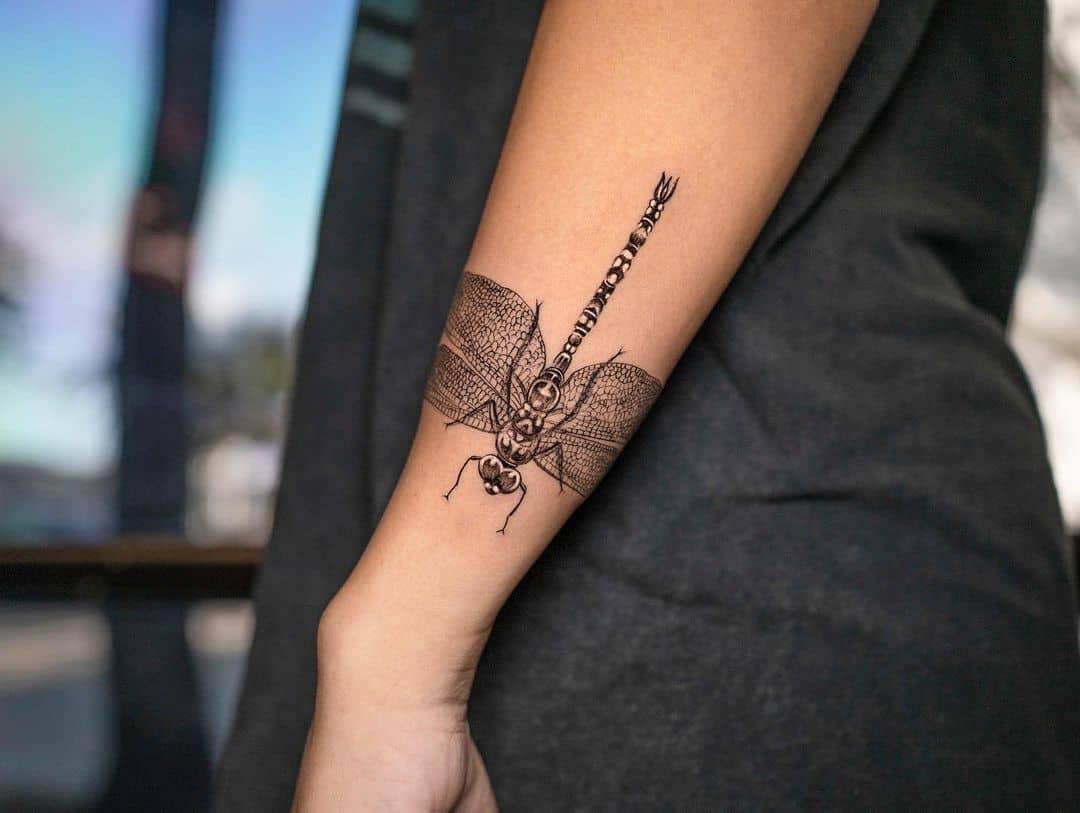 Tatuaje en el brazo, libélula negra detallada